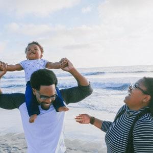 A family on the beach joyfully lifts their child up, creating a heartwarming moment of togetherness and happiness.