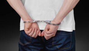 A man with his hand in handcuffs behind his back, wondering about the differences between Maryland public defenders and private attorneys.