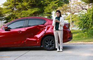 A woman standing next to her dented car, on the phone, dealing with an insurance adjuster in Maryland.